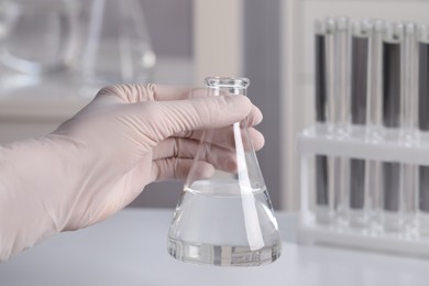 Photo of Scientist holding conical flask with transparent liquid in laboratory, closeup