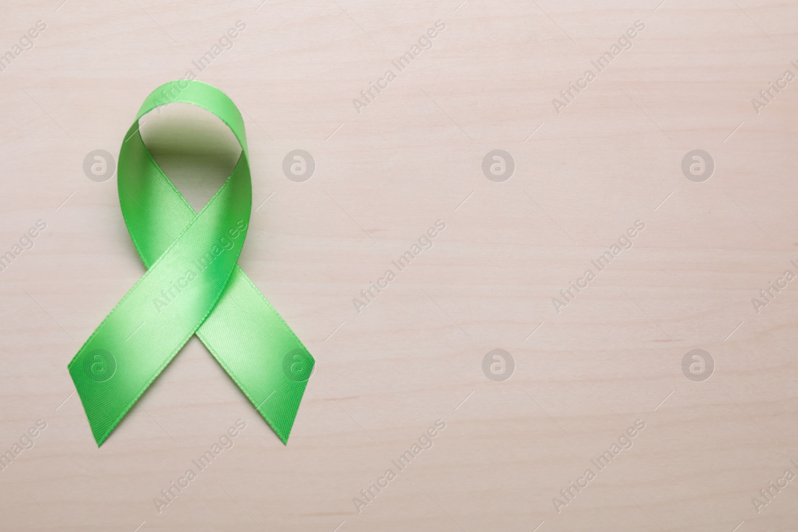 Photo of World Mental Health Day. Green ribbon on wooden background, top view with space for text