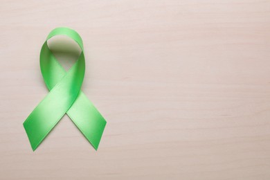 Photo of World Mental Health Day. Green ribbon on wooden background, top view with space for text