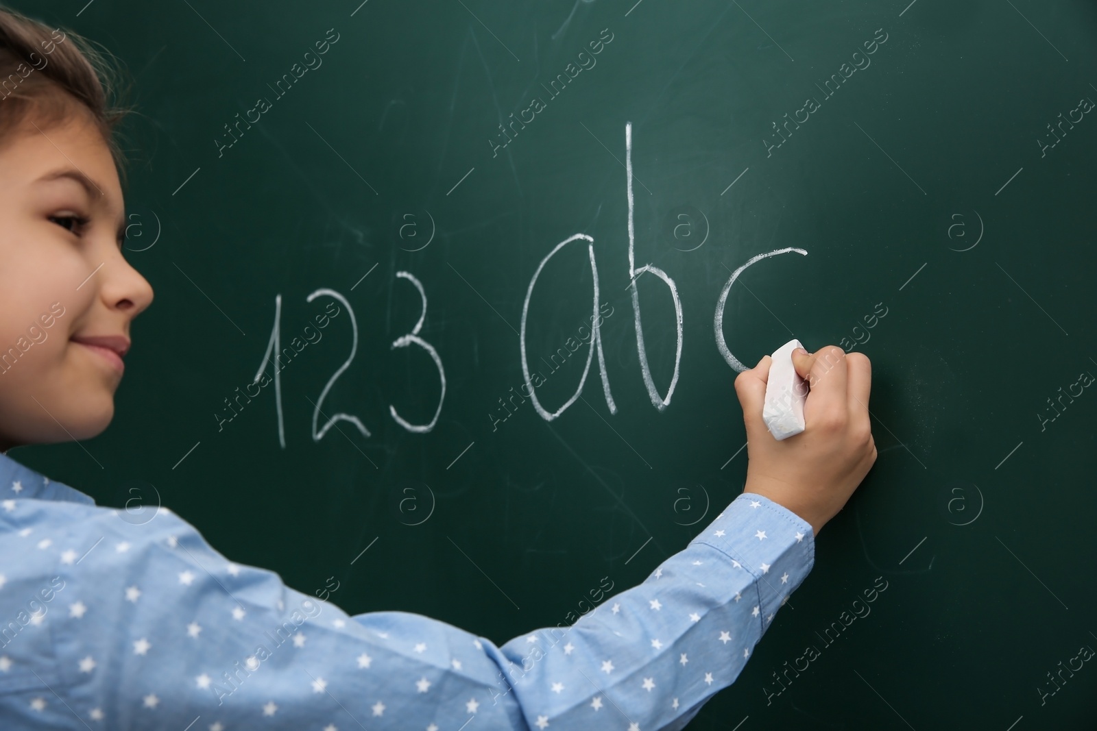 Photo of Little child writing letters and numbers on chalkboard