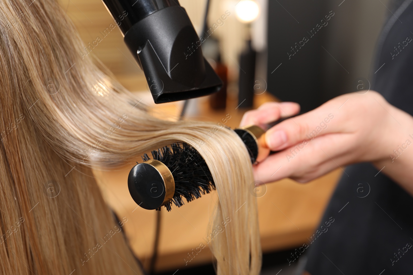 Photo of Hairdresser blow drying client's hair in salon, closeup