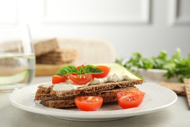 Photo of Fresh rye crispbreads with cream cheese and vegetables on light grey table, closeup