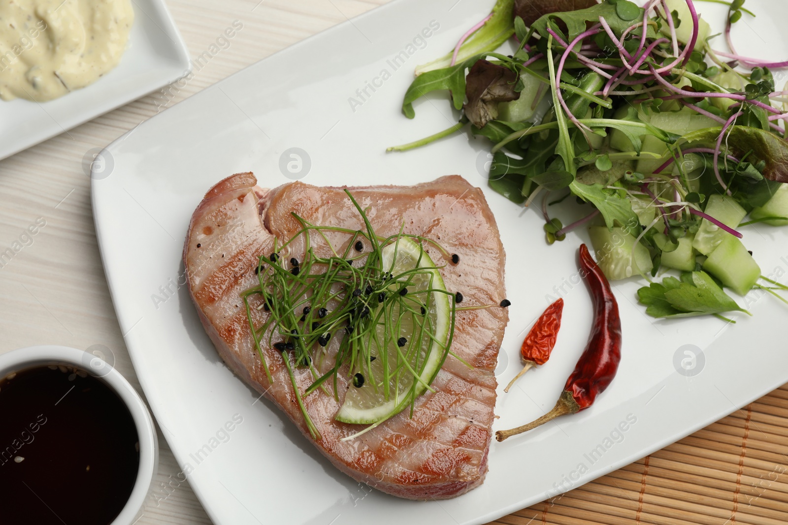 Photo of Delicious tuna steak served with salad and sauces on white wooden table, flat lay