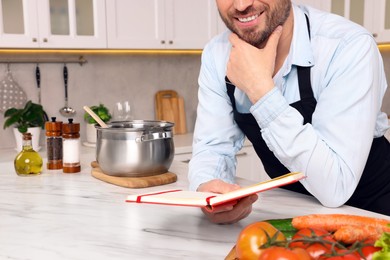 Photo of Man with recipe book at white marble table in kitchen, closeup