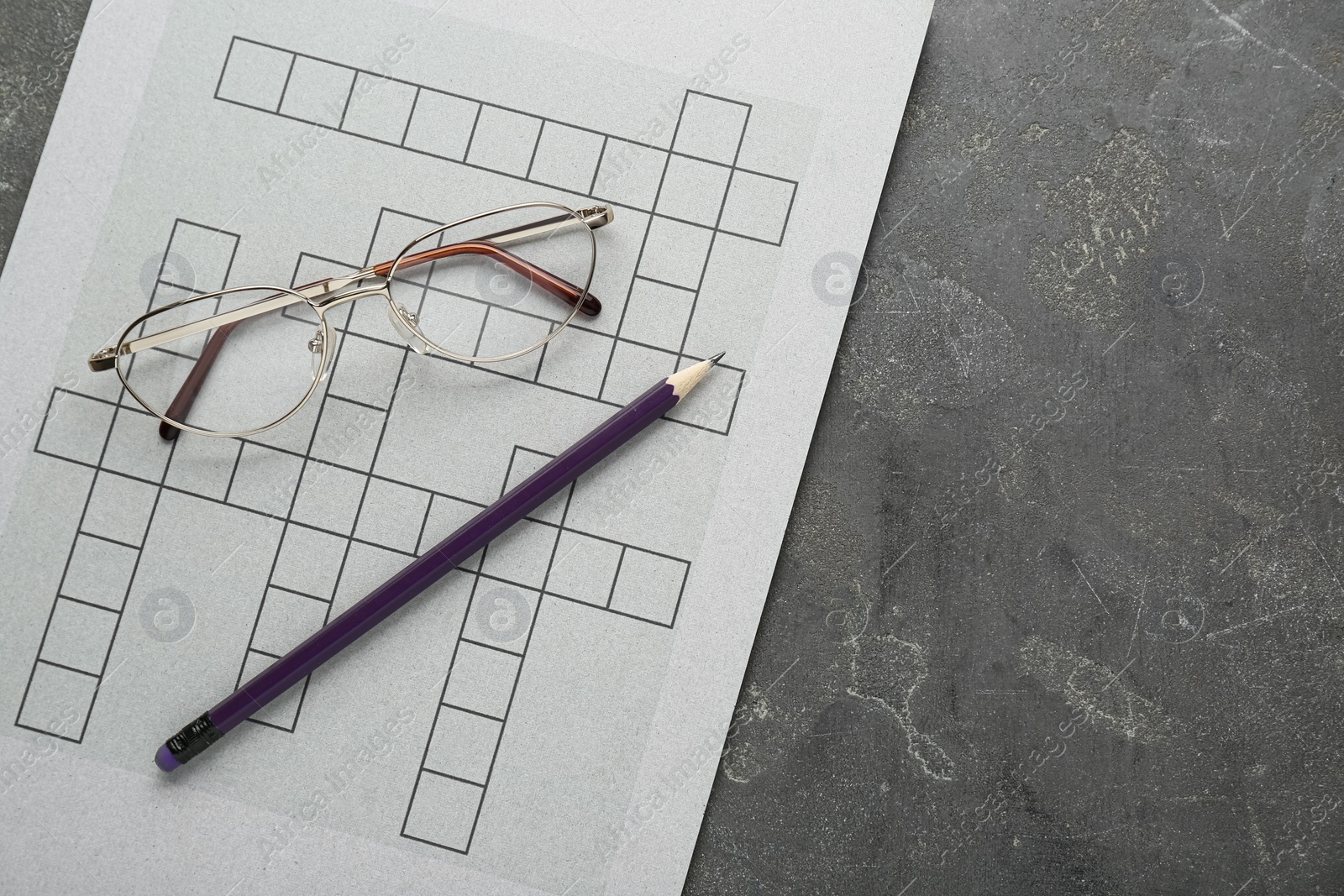 Photo of Blank crossword, glasses and pencil on grey table, top view. Space for text