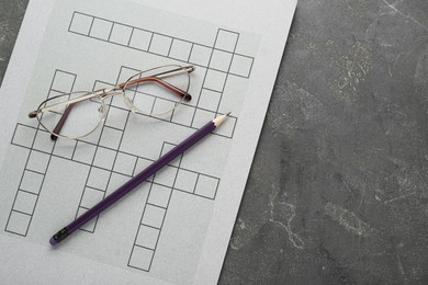 Blank crossword, glasses and pencil on grey table, top view. Space for text