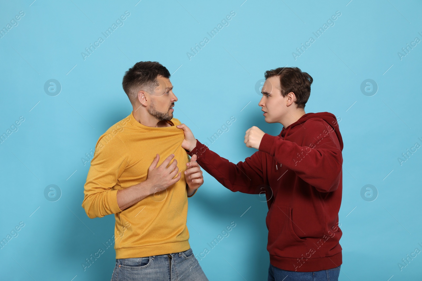 Photo of Two emotional men fighting on light blue background