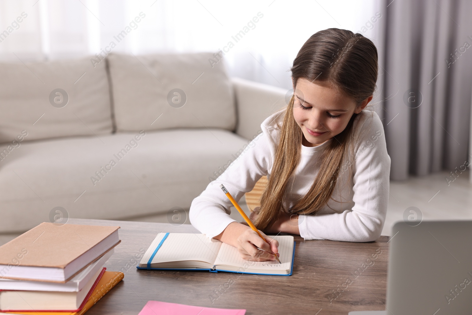 Photo of E-learning. Cute girl taking notes during online lesson at table indoors