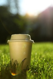 Photo of Cardboard takeaway coffee cup with lid on green grass outdoors, space for text