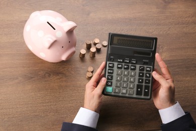 Photo of Budget planning. Businessman with piggy bank calculating at wooden table, closeup