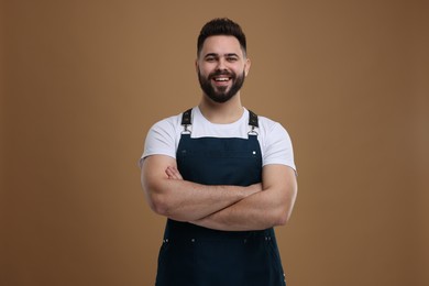 Photo of Smiling man in kitchen apron with crossed arms on brown background. Mockup for design