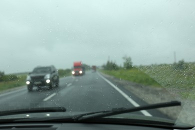 Photo of Blurred view of country road through wet car window. Rainy weather