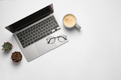 Modern laptop, houseplants, glasses and cup of coffee on white table, flat lay. Space for text