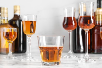 Photo of Delicious liqueurs in glasses and bottles on white marble table