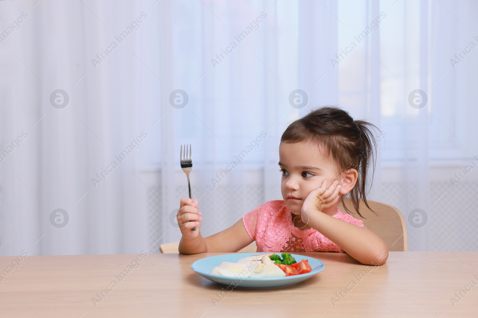 Photo of Cute little girl refusing to eat her breakfast at home, space for text