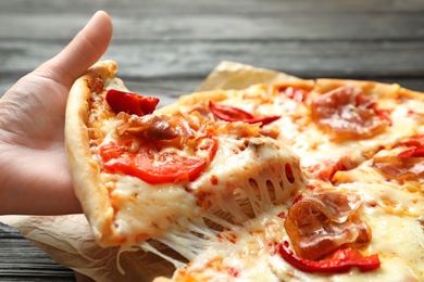 Photo of Woman holding slice of delicious hot pizza over table, closeup