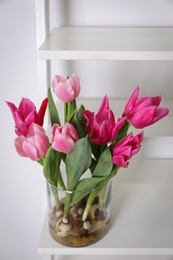 Photo of Beautiful tulips with bulbs on decorative ladder near white wall