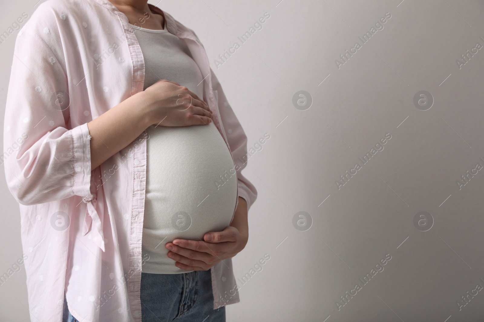 Photo of Young pregnant woman on light grey background, closeup. Space for text