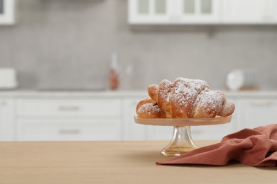 Photo of Stand with delicious croissants and napkin on table in kitchen, space for text