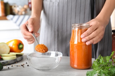 Photo of Woman with jar of pickled squash spread at grey marble table indoors