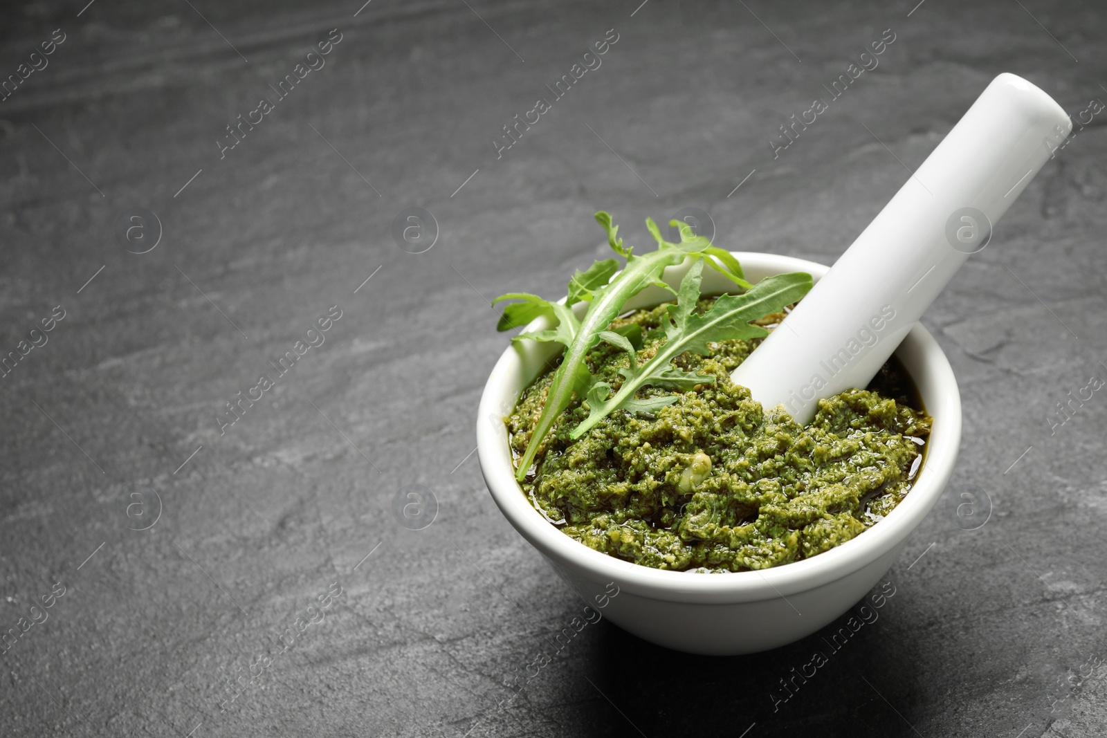 Photo of Mortar with tasty arugula pesto on black table. Space for text