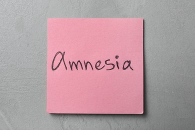 Photo of Note with word Amnesia on light grey table, top view