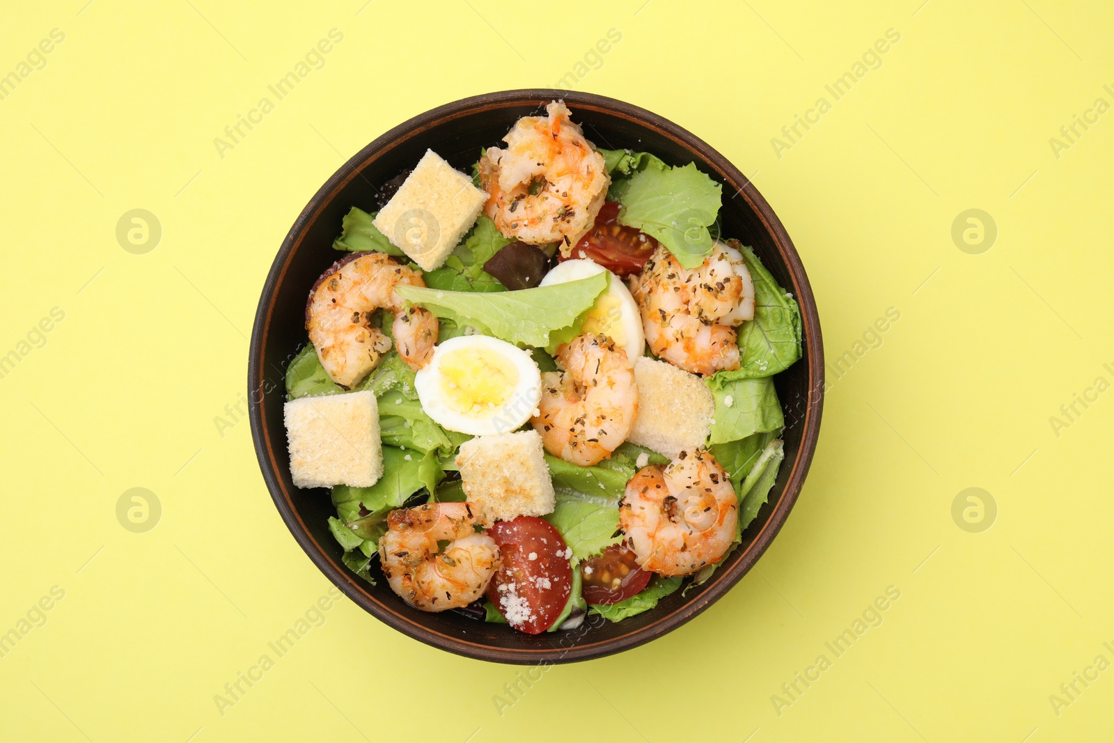 Photo of Delicious Caesar salad with shrimps on yellow background, top view