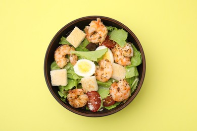 Photo of Delicious Caesar salad with shrimps on yellow background, top view