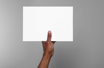 Photo of African American man holding sheet of paper on grey background, closeup. Mockup for design