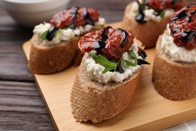 Photo of Delicious bruschettas with sun-dried tomatoes, cream cheese and balsamic vinegar on wooden table, closeup