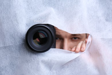 Photo of Hidden man with camera spying through hole in white fabric, closeup
