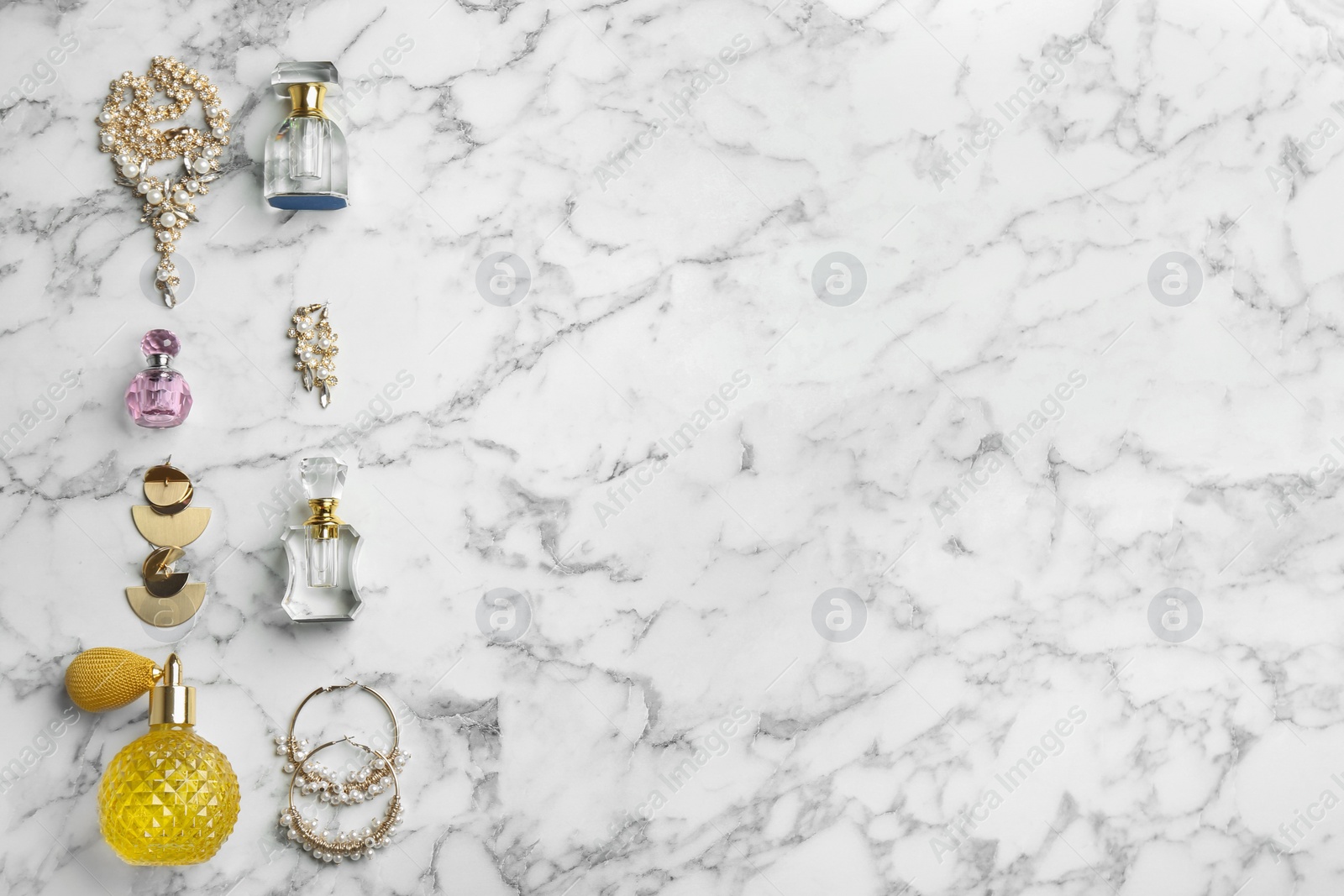 Photo of Flat lay composition with perfume bottles and jewelry on white marble table, space for text