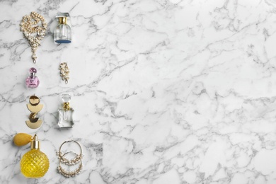 Flat lay composition with perfume bottles and jewelry on white marble table, space for text