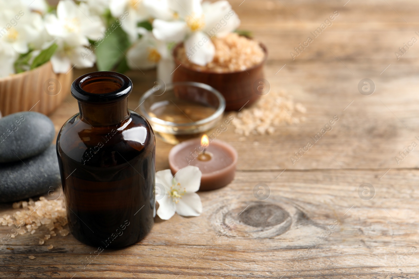 Photo of Beautiful composition with jasmine essential oil and fresh flowers on wooden table. Space for text