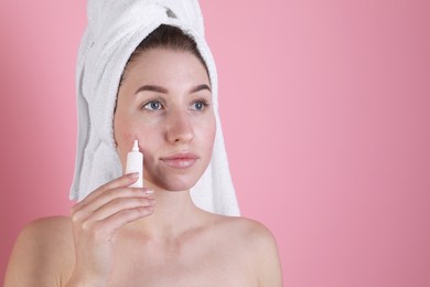 Photo of Young woman with acne problem applying cosmetic product onto her skin on pink background. Space for text