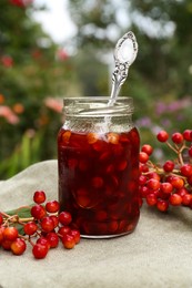 Photo of Jar of tasty jam and viburnum berries on table outdoors
