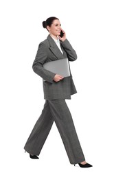 Photo of Beautiful happy businesswoman with laptop talking on smartphone while walking against white background