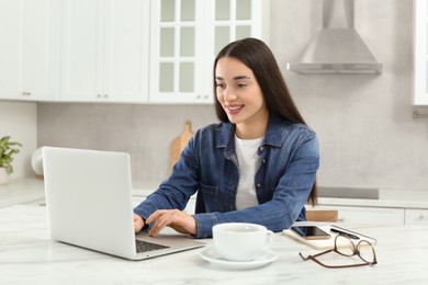 Home workplace. Happy woman typing on laptop at marble desk in kitchen