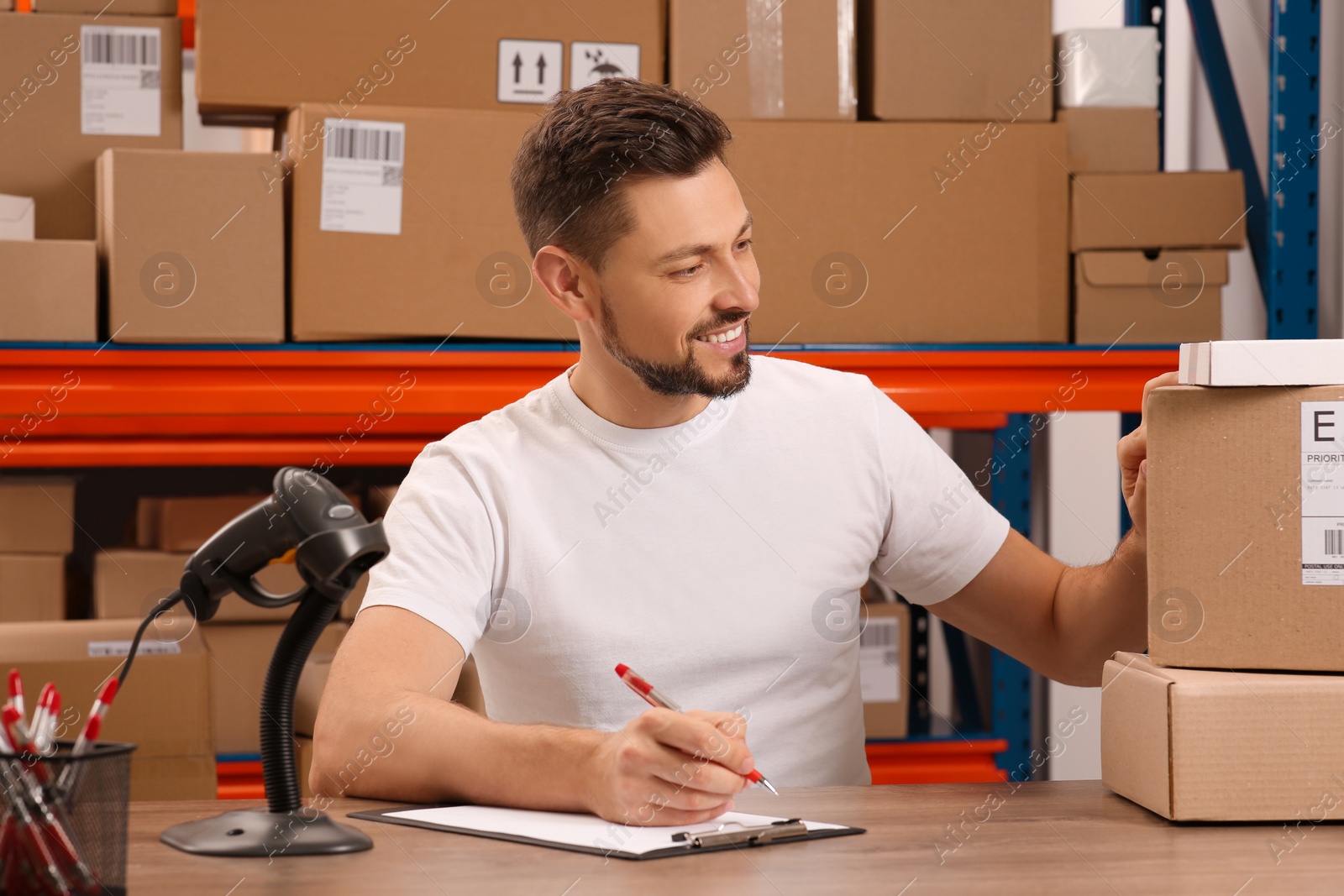 Photo of Post office worker with clipboard and parcels at counter indoors