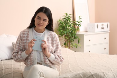 Photo of Young woman with greeting card on bed in room, space for text