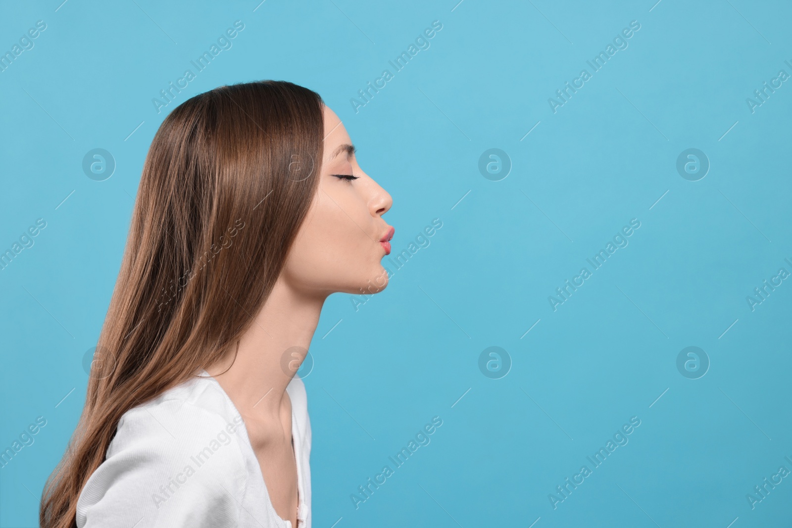 Photo of Beautiful young woman blowing kiss on light blue background, space for text