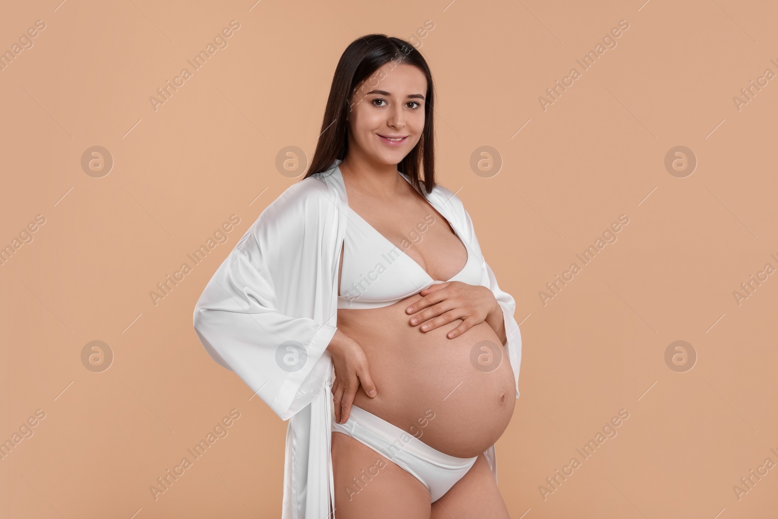 Photo of Beautiful pregnant woman in stylish comfortable underwear and robe on beige background