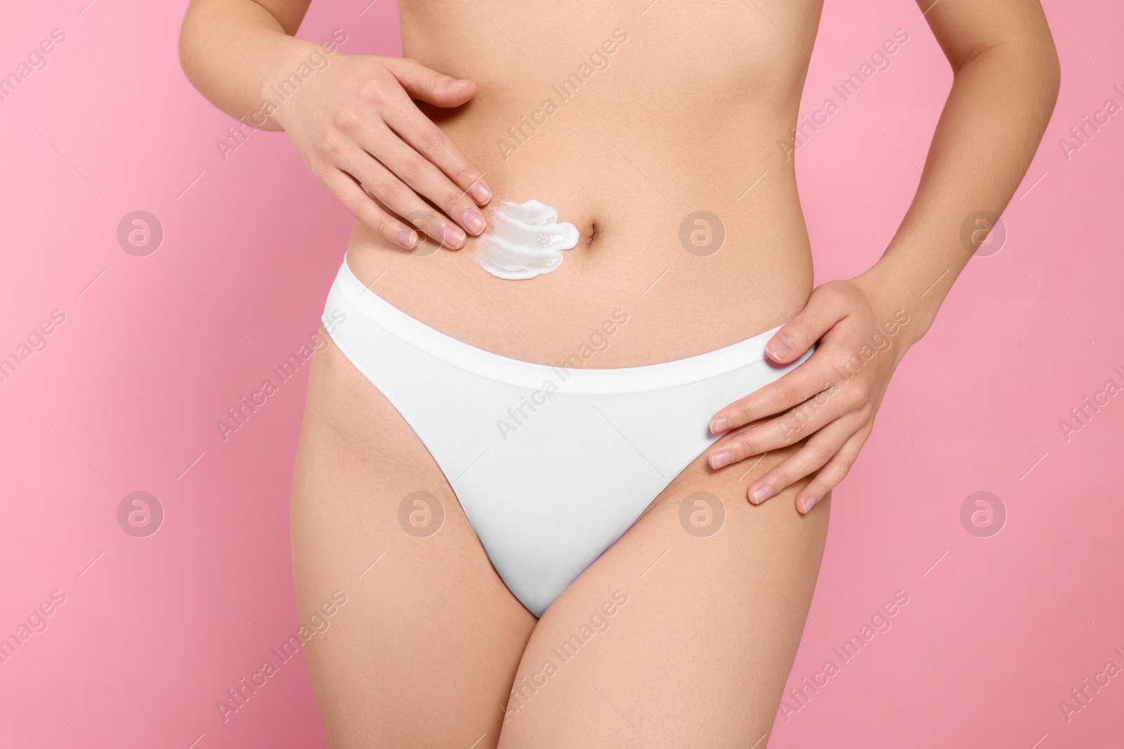 Photo of Woman applying body cream on belly against pink background, closeup