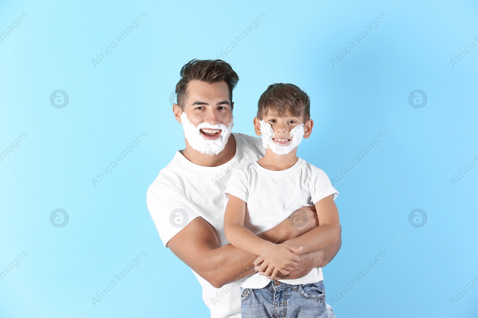 Photo of Father and son with shaving foam on faces against color background