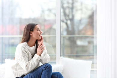 Photo of Young woman in sweater sitting near window indoors