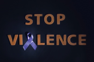 Purple awareness ribbon and phrase STOP VIOLENCE made of wooden letters on black background, top view