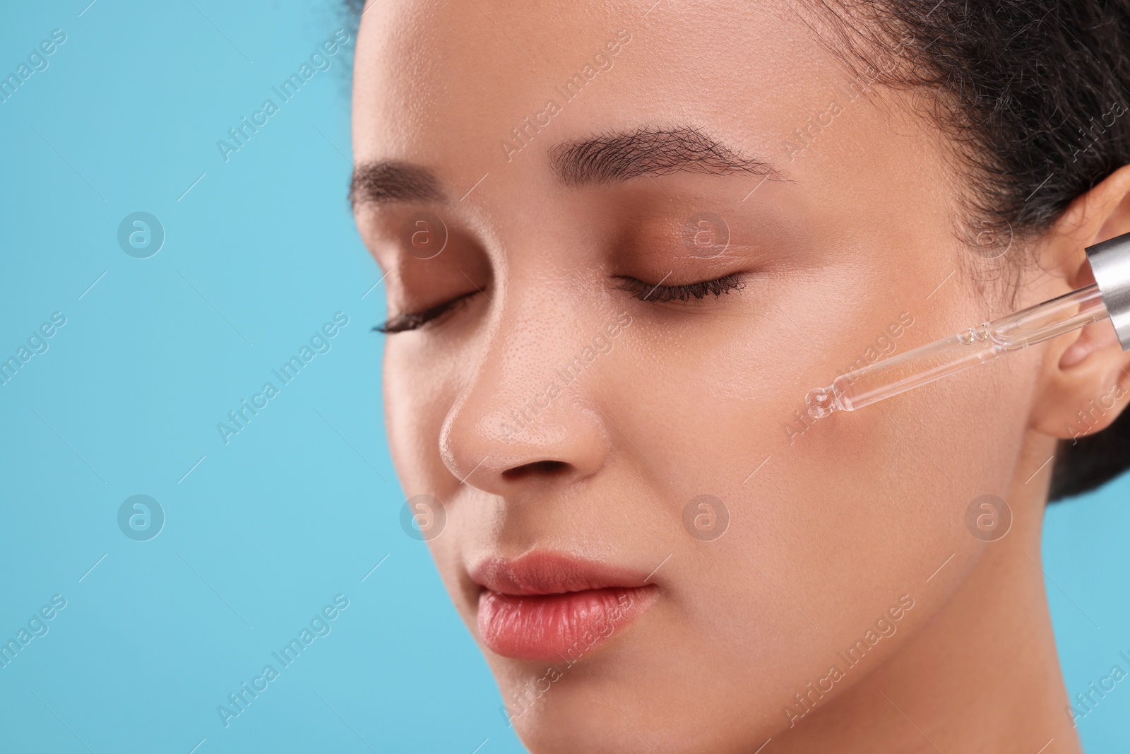 Photo of Beautiful woman applying serum onto her face on light blue background, closeup. Space for text