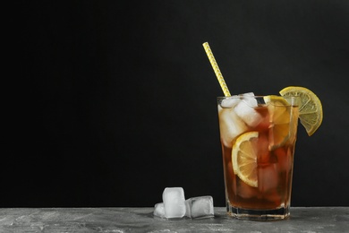 Photo of Glass of delicious iced tea on grey table against black background. Space for text