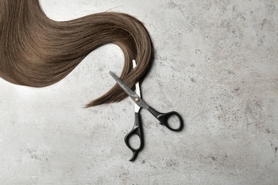 Hair lock and scissors on grey background, top view. Space for text