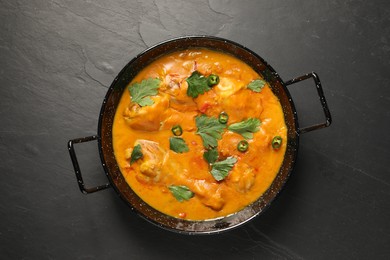 Tasty chicken curry with parsley and pepper on black textured table, top view